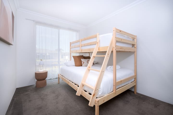 Chambre confortable avec un lit superposé en bois avec un matelas double en bas et une chambre simple sur le dessus, parfaite pour les familles ou les groupes. La grande fenêtre permet une lumière naturelle, avec une table de chevet et des accents décoratifs moelleux.