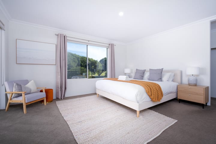 Chambre spacieuse et sereine avec un lit queen size confortable avec des draps moelleux, accentué par un jet orange confortable. La grande fenêtre offre une vue panoramique, et un fauteuil élégant fournit un coin lecture.