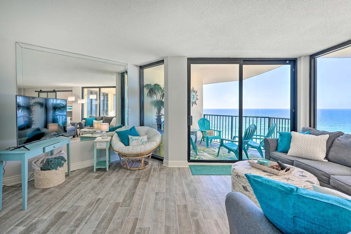 A modern living area features large glass doors that lead to a private balcony with ocean views. Comfortable seating arrangements, including a plush sofa and a cozy chair, are accented with decorative pillows. Natural light fills the space, highlighting the neutral flooring and coastal-themed decor.