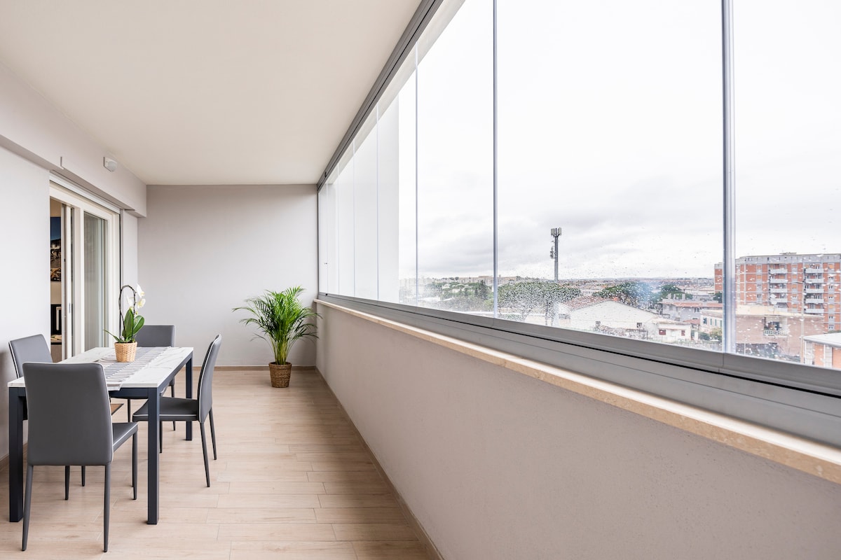 A spacious balcony features large sliding glass doors that offer ample natural light. A dining table with comfortable chairs sits adjacent to a potted plant, creating an inviting space for meals or relaxation with views of the surrounding area.
