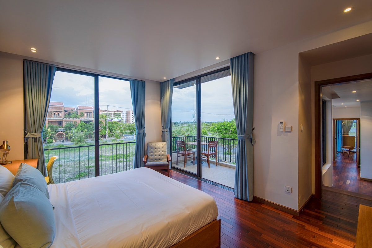 The second-floor bedroom boasts a lavish king-sized bed and an open window that frames a breathtaking landscape view, adding a touch of tranquility and natural beauty to the elegant space