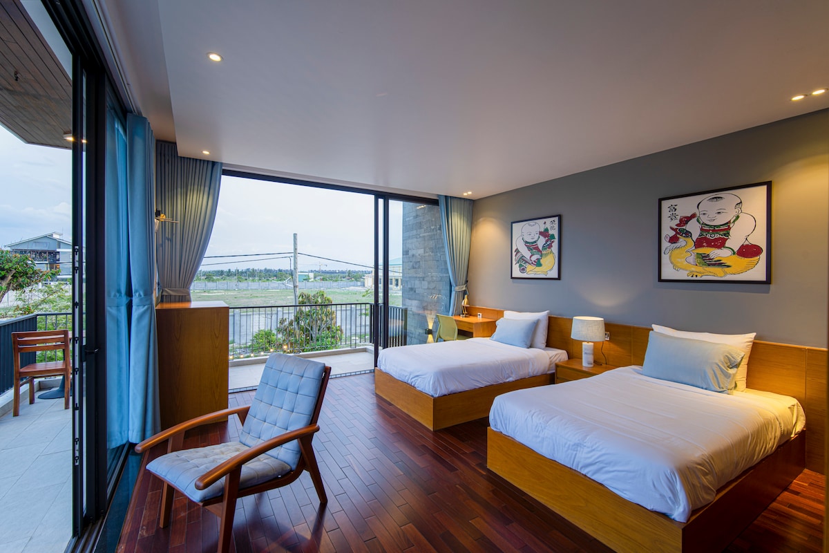 The alternate second-floor bedroom offers a spacious 2 single - sized beds and an open window revealing a stunning landscape view, bringing nature's beauty into this cozy and comfortable retreat.