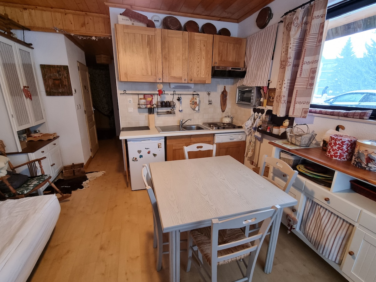 A fully equipped kitchen is presented with wooden cabinetry, a stove, and a microwave. A light-colored dining table with four chairs offers a communal space. Various kitchen utensils and decorative elements enhance the practical atmosphere, with natural light filtering through a nearby window.