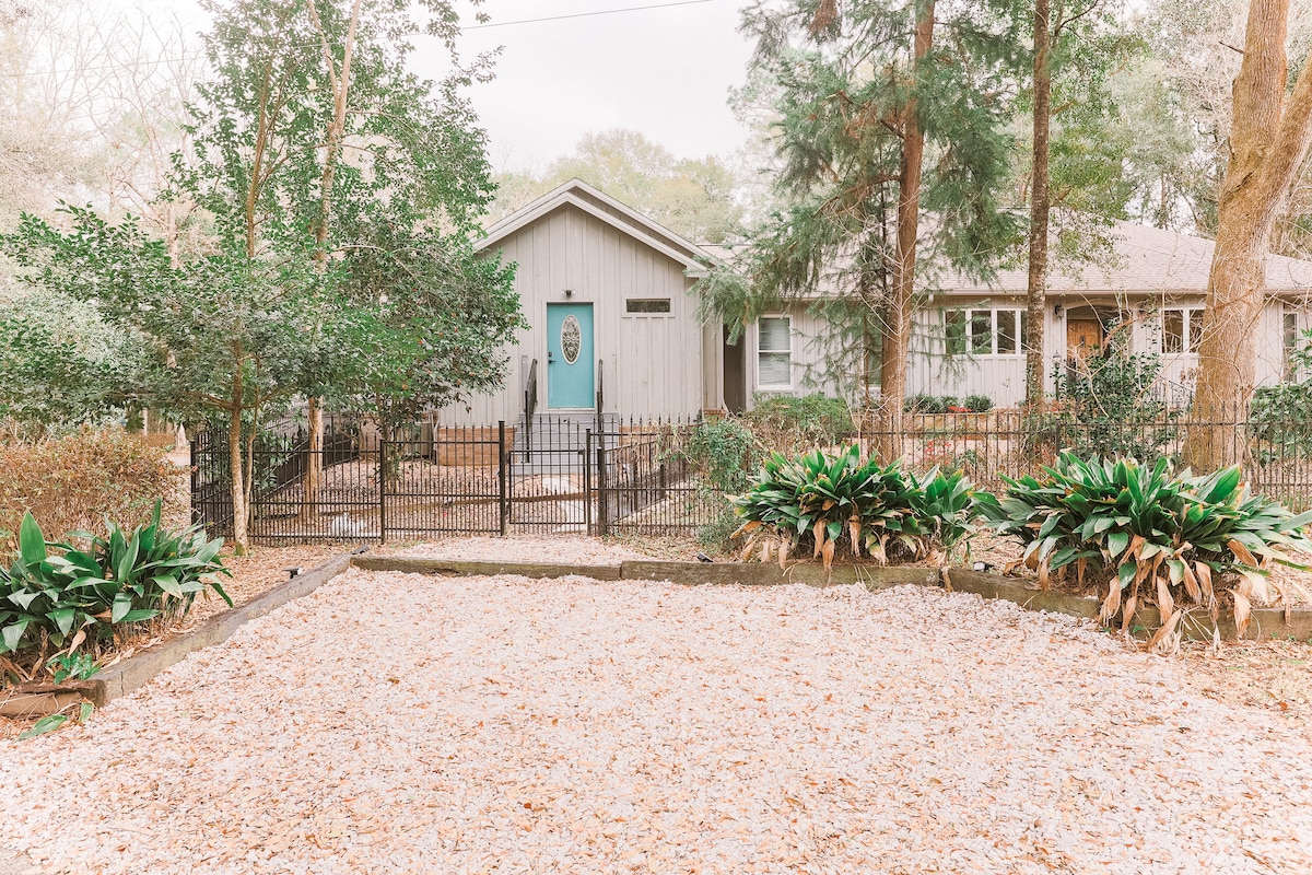 The exterior view features a modern guest house surrounded by a neatly landscaped yard. A gravel pathway leads to a welcoming front door framed by lush greenery and well-maintained shrubs. A wrought-iron fence encloses the property, providing a sense of privacy.