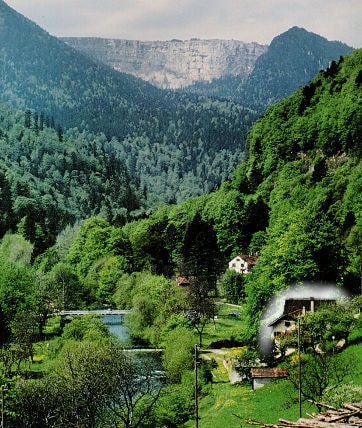 A serene landscape is captured, showing a lush green valley surrounded by towering mountains. A river gently flows through the scene, with a quaint house nestled among the trees, highlighting the peacefulness of the natural environment.