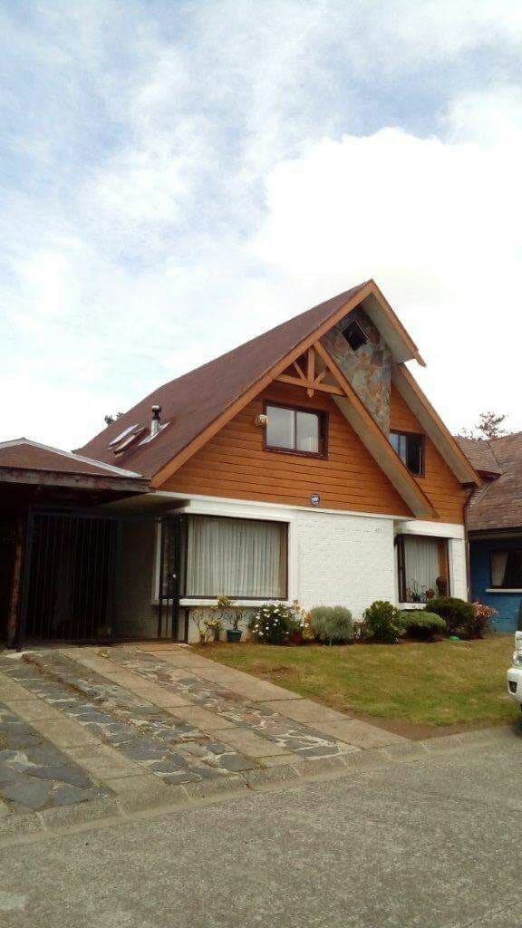 A charming two-story house features a combination of wood and stone accents. Large windows allow natural light to fill the space, while a neatly landscaped garden offers colorful flowers and greenery. The sloped roof adds to the home's character, set against a cloudy sky.