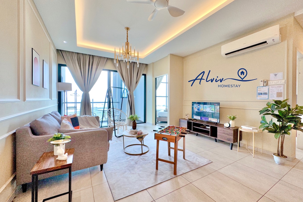 The living area features a comfortable sofa and a TV on a wooden stand. A round coffee table sits in the center, complemented by a small dining table. Natural light fills the space through large windows, enhancing the inviting atmosphere.
