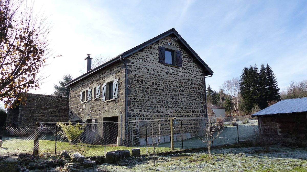 A traditional stone barn is visible, showcasing a rustic exterior with multiple windows. The structure is set against a clear sky, surrounded by a grassy area and scattered trees, indicating a serene countryside location.