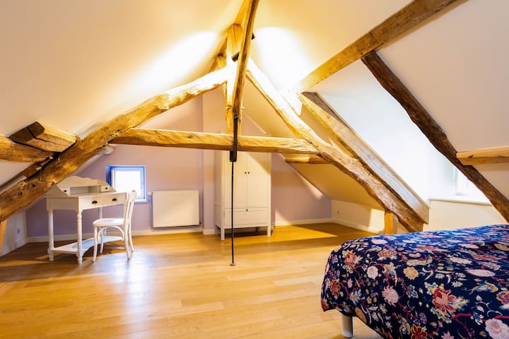 La chambre sous les toits ! Située au 2ᵉ étage, cette chambre atypique, avec ses poutres apparentes d'époques, vous ravira par sa grandeur et son charme. Cette chambre vous offre une coiffeuse, des rangements, un lit douillet et vue sur le jardin. 
