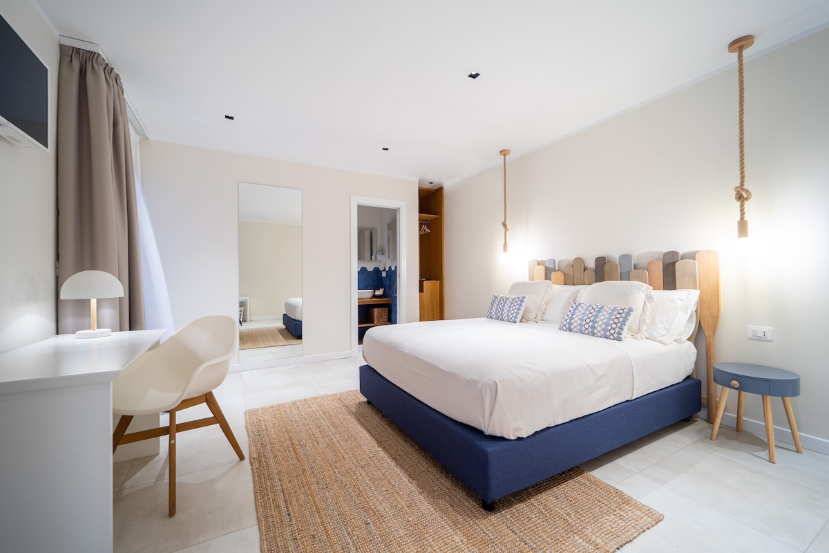 Panoramica room con letto queen - size, armadio , ingresso bagno, scrivania e TV LED HD