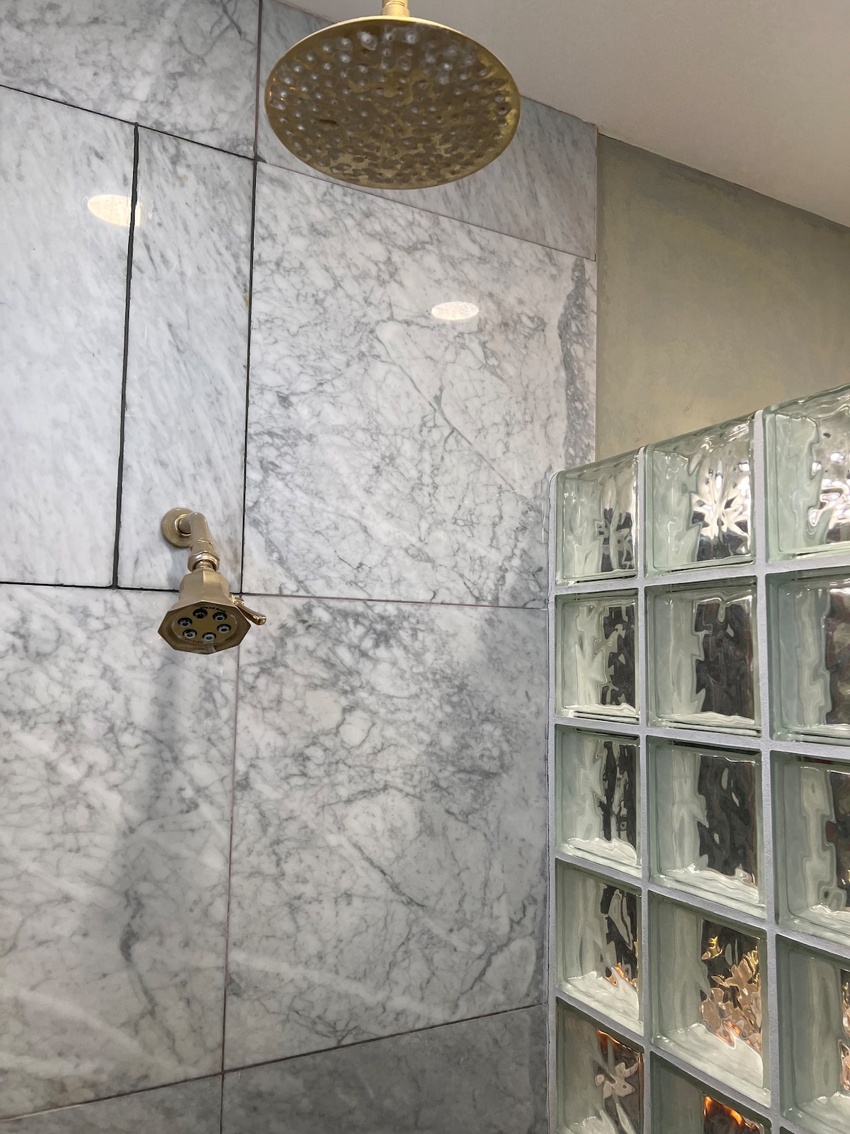 A modern en suite bathroom is featured, showcasing elegant marble walls and a glass block shower enclosure. A stylish showerhead is mounted on the wall, complementing the sophisticated design. Soft lighting enhances the space, creating a serene atmosphere.