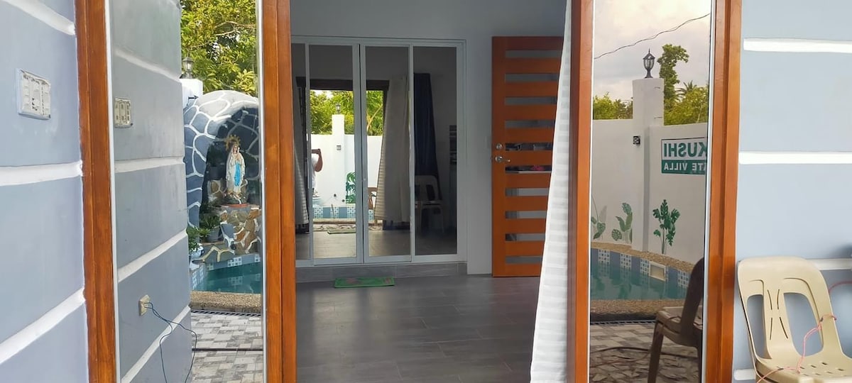 A spacious entrance opens to a living area with large sliding glass doors, providing a view of an outdoor dipping pool. A wooden door with decorative panels adds character. The flooring is tiled, and soft natural light fills the interior.