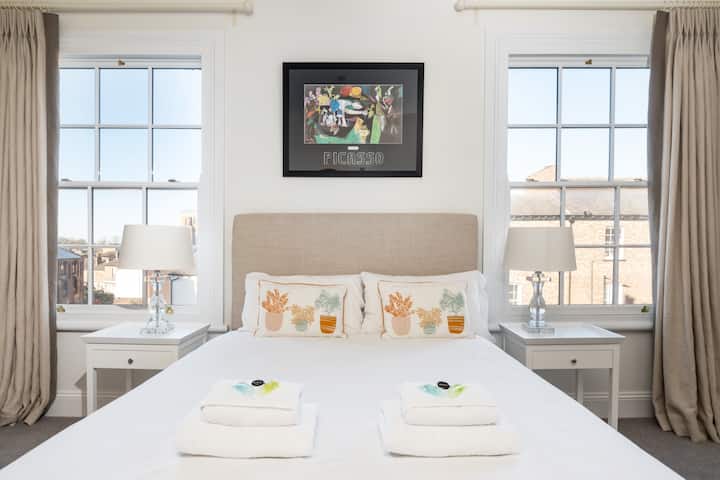 ห้องนอนใหญ่พร้อมเตียงคู่ล้อมรอบด้วยหน้าต่างสูง 2 บานที่สวยงาม