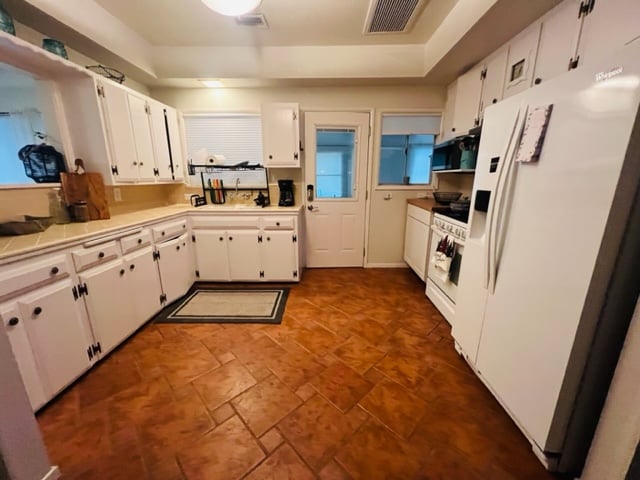 A well-organized kitchen features a blend of white cabinetry and a spacious countertop. Stainless steel appliances are positioned for convenience, while a door leads to an exit, enhancing accessibility. Attractive tile flooring adds warmth to the overall space.