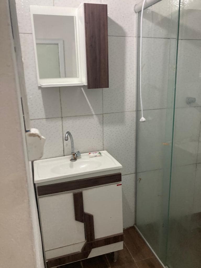 A modern bathroom features a compact vanity with a sink and storage cabinet. A clear glass shower enclosure offers a streamlined look, while light tiles and wood-look flooring contribute to a clean and functional atmosphere.