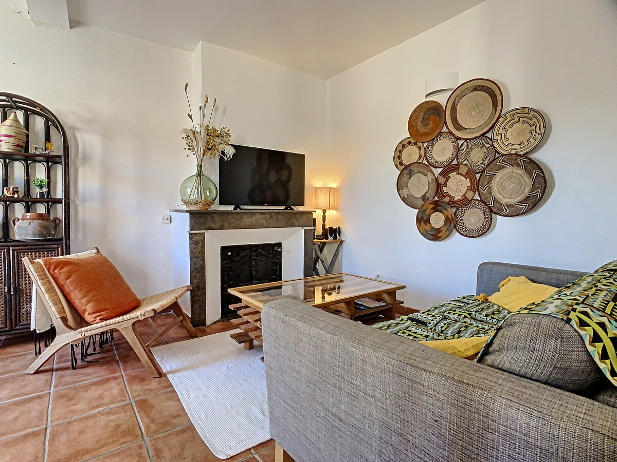 A comfortable living area is showcased, featuring a sofa adorned with colorful cushions. A coffee table occupies the center, while unique wall decor made of woven baskets adds visual interest. A television sits above a decorative fireplace, enhancing the room's cozy atmosphere.