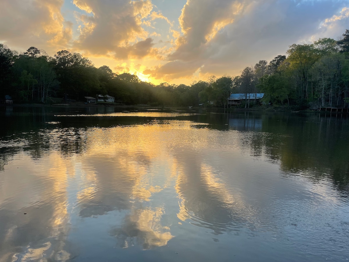 The tranquil surface of Southwood Lake reflects a vibrant sunset, with hues of orange and gold mingling in the water. Silhouettes of trees and nearby cabins frame the horizon, enhancing the serene atmosphere of this private lakeside retreat.