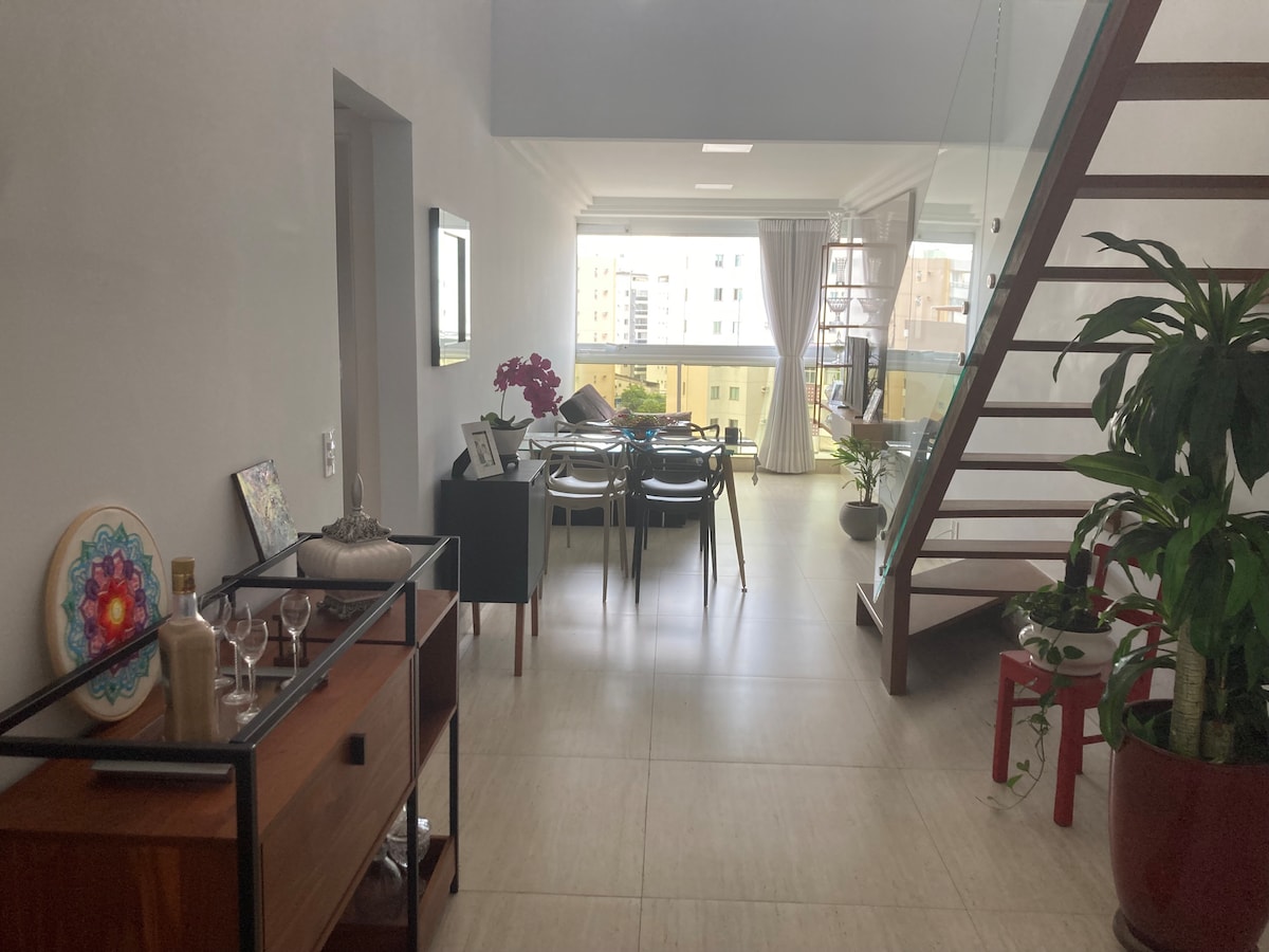 Sala de TV con sofá retráctil y mesa con 4 sillas y cortina opaca.