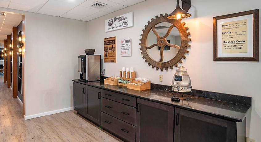 A welcoming communal area features a dark countertop with serving essentials, accompanied by a vintage gear wall decoration. The space is illuminated by pendant lighting, creating a functional and inviting environment for guests.