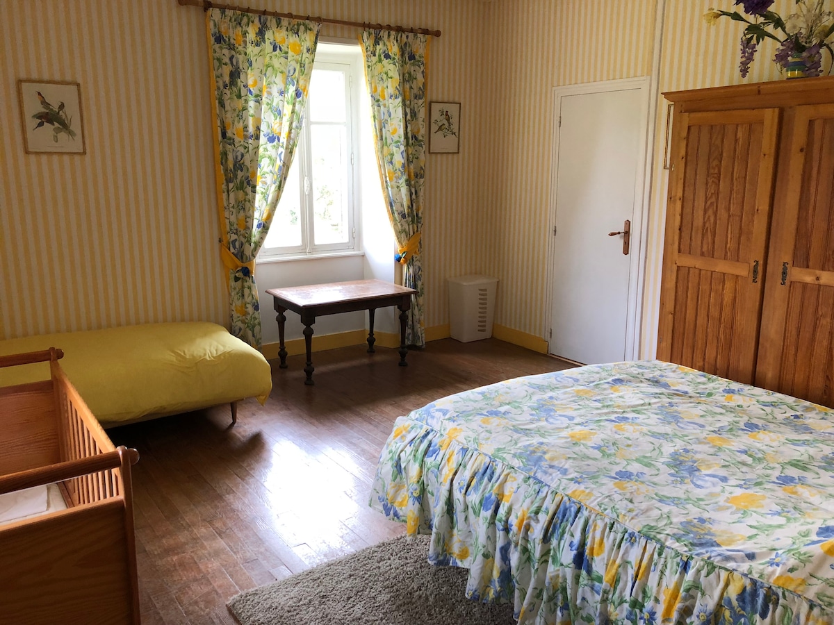 חדר שינה צהוב בבית הגדול עם מיטה זוגית, מיטת יחיד ועריסה. 