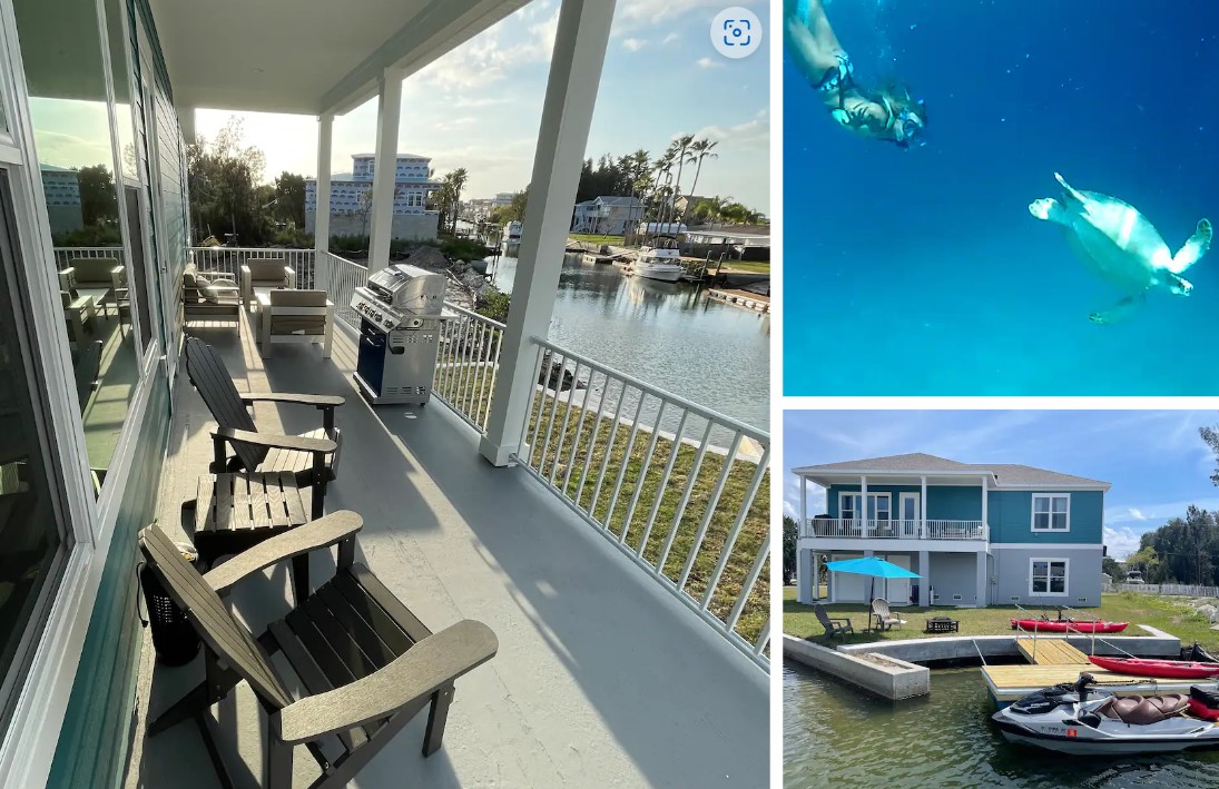 The spacious outdoor deck features comfortable seating with two Adirondack chairs and a gas grill, overlooking the water. The property is set in a serene environment, surrounded by lush greenery and gentle waves. Multiple kayaks and paddleboards are visible at the water's edge.