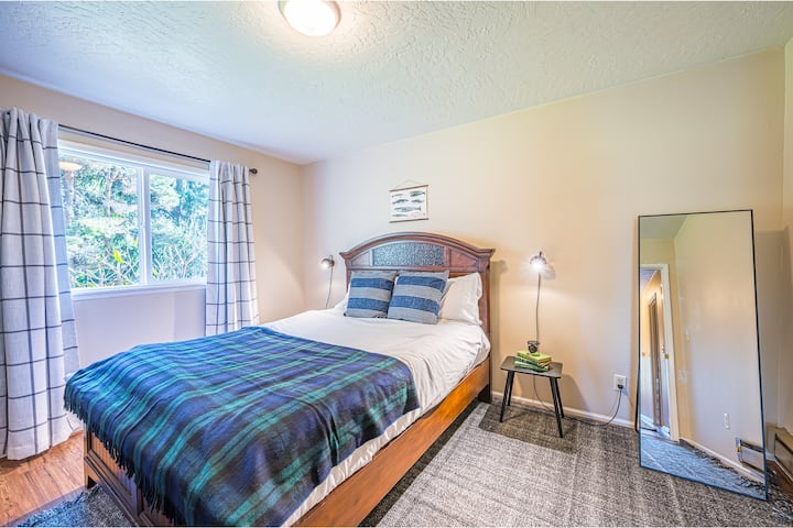 Chumba cha kulala cha pili kilicho na kitanda cha malkia, matandiko ya chini, mapazia meusi, taa za kando ya kitanda na kabati.