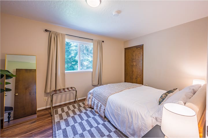 Chumba cha kulala cha tatu kilicho na kitanda cha malkia, matandiko ya chini, mapazia meusi, taa za kando ya kitanda, kabati.