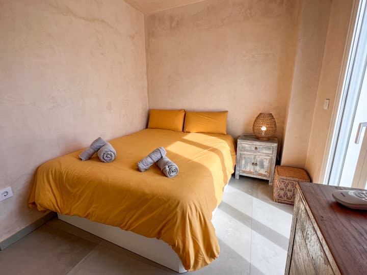 Mwonekano wa jumla wa chumba. Mwangaza wa asili. Kitanda cha sentimita 150 kilichovaa mashuka bora. Taulo 100% za pamba. Mesilla na meza thabiti ya kuvaa mbao. Taa ya meza na puff ya nyuzi za asili. Kiyoyozi.