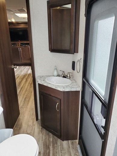A compact bathroom features a sink with a marble countertop and a mirror above. Light wood cabinetry offers storage space below. A sliding glass door provides access to the outside, while wood-like flooring enhances the overall aesthetic.