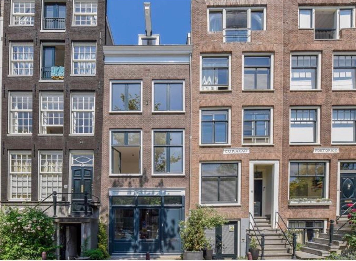 A stylish canal house is presented, featuring a brick façade with large windows that provide ample natural light. The entrance is framed by greenery, enhancing the building's character. Steps lead up to the front door, emphasizing the property's welcoming appeal in Amsterdam's vibrant architecture.