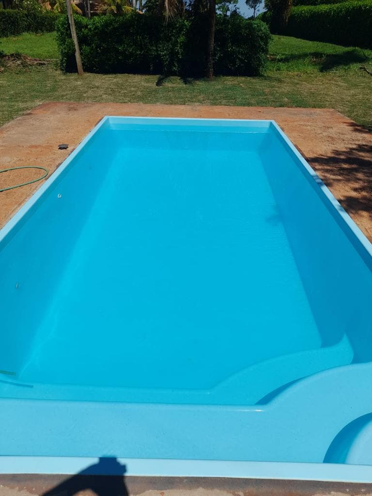 A clear, turquoise swimming pool is set against a backdrop of green grassy areas and trees. The pool's smooth edges and shallow entry point are visible, inviting relaxation and enjoyment. Sunlight reflects off the water's surface, enhancing its inviting appearance.