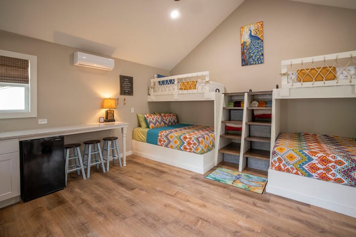BUNK HOUSE (view 1).  Very open space with custom built in bunks (twin over queen).   The steps between the bunks are also storage for the bath towels and blankets.  Here you can see the mini fridge and a few stools for seating.  Split AC unit.