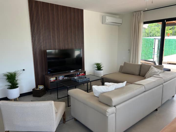 Sebule angavu iliyo na sofa kubwa, televisheni janja na kiyoyozi, bora kwa ajili ya kupumzika baada ya ufukweni.