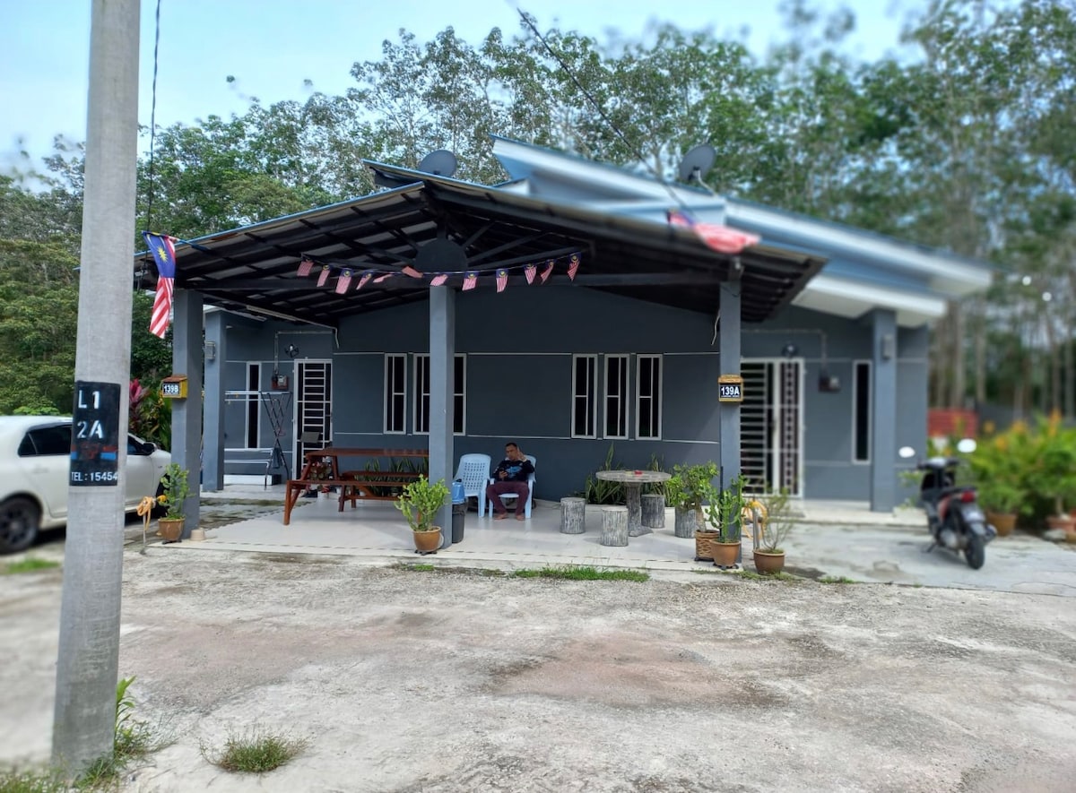 A modern single-story building features a covered porch area with seating arrangements. Surrounding greenery adds a natural touch, while potted plants are positioned along the patio. The driveway accommodates a vehicle, and decorative elements, including flags, enhance the welcoming appearance of the entrance.