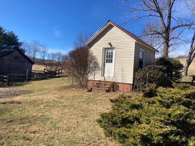A quaint cottage is nestled within a natural landscape, featuring a light-colored exterior and a simple front porch. Surrounding greenery includes well-maintained shrubs and a flat lawn, with rolling pastures visible in the background under a clear blue sky.