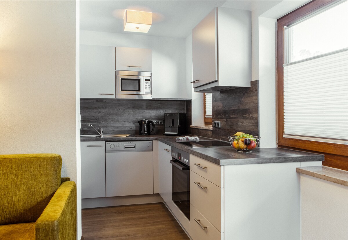 A modern kitchen area is equipped with sleek cabinetry and stainless steel appliances. A built-in microwave and oven are neatly integrated. A bowl of fruit sits on the countertop, highlighting the space’s functionality and inviting atmosphere.