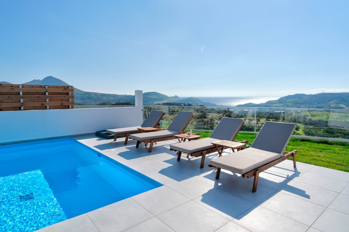 A private pool area is highlighted with four lounge chairs arranged around the verdant landscape and expansive sea view. The pool's clear water reflects the serene blue sky, creating a harmonious outdoor space for relaxation.