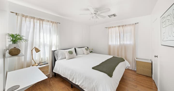 Hotel-quality king mattress on gray platform bed. 100% cotton premium sheets in white. Down alternative comforter with comforter protector and duvet cover. Pillow covers and protectors. Olive colored premium cotton throw blanket, wicker hamper. 