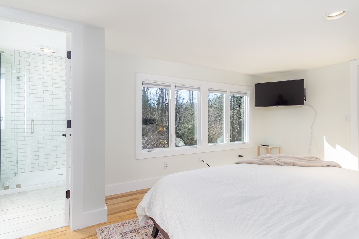 Televizor i montuar në mur me dritare të mëdha që shikojnë në oborrin e pasmë.