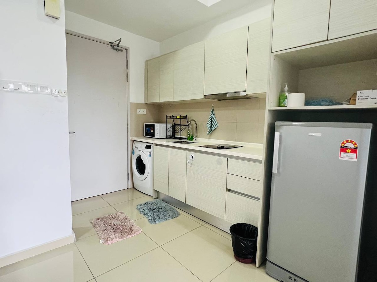 A modern kitchen is shown, featuring light-colored cabinetry and a compact layout. Essential appliances include a washing machine, refrigerator, and stove. A sink with a dish rack is visible, along with a small mat on the floor. Clean lines and a neutral color palette create a functional space.
