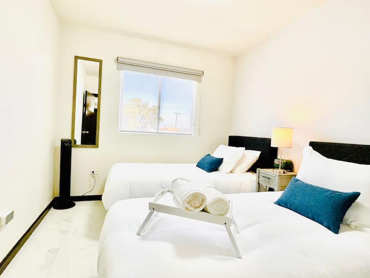 Recámara con 2 camas individuales, con colchones memory foam para mayor comodidad. Incluye lámpara de noche, ventilador de torre, espejo de cuerpo completo y una bandeja de bienvenida con toallas. Espacio ideal para niños o amigos que viajan juntos.