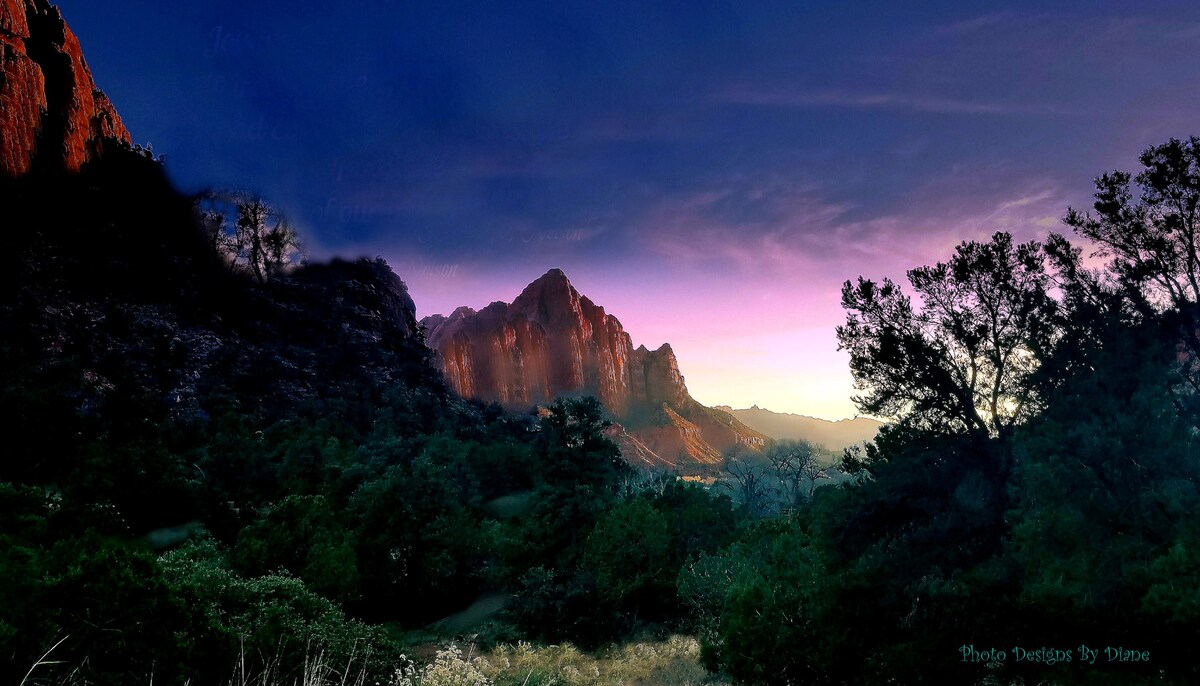 A panoramic view captures the majestic mountains under a twilight sky. Soft shades of purple and orange illuminate the peaks, while lush greenery is present in the foreground, adding depth to the serene landscape.
