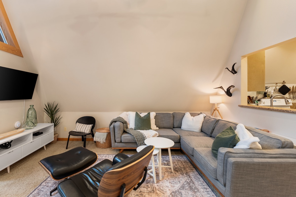 Hapa unaona sebule ya ghorofa ya juu iliyo karibu na jiko na sehemu ya kula. Ina televisheni kwa ajili ya burudani yako. Kochi kubwa la sehemu ni mahali pazuri pa kukusanyika kwa ajili ya usiku wa sinema au kukumbuka kuhusu jasura nzuri.