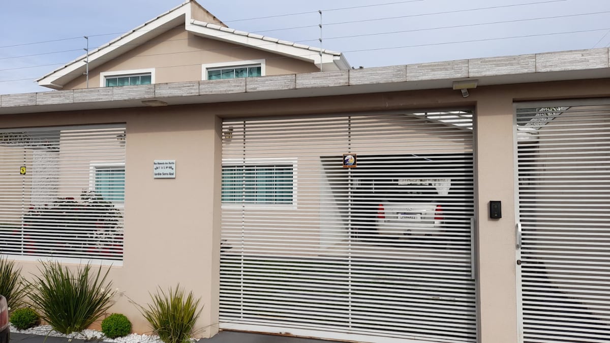 The exterior of the property features a well-maintained facade with horizontal blinds, providing privacy. A spacious garage is visible, accommodating multiple vehicles. The landscaped area includes small shrubs, enhancing the entrance. The upper level of the house showcases large windows that invite natural light.