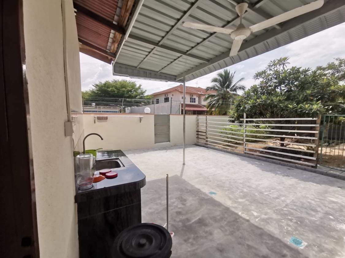An outdoor area is shown with a functional sink and countertop, designed for convenience. A large awning provides shade over the space, surrounded by a low fence and greenery. Concrete flooring enhances the practicality of the area, making it suitable for gatherings.