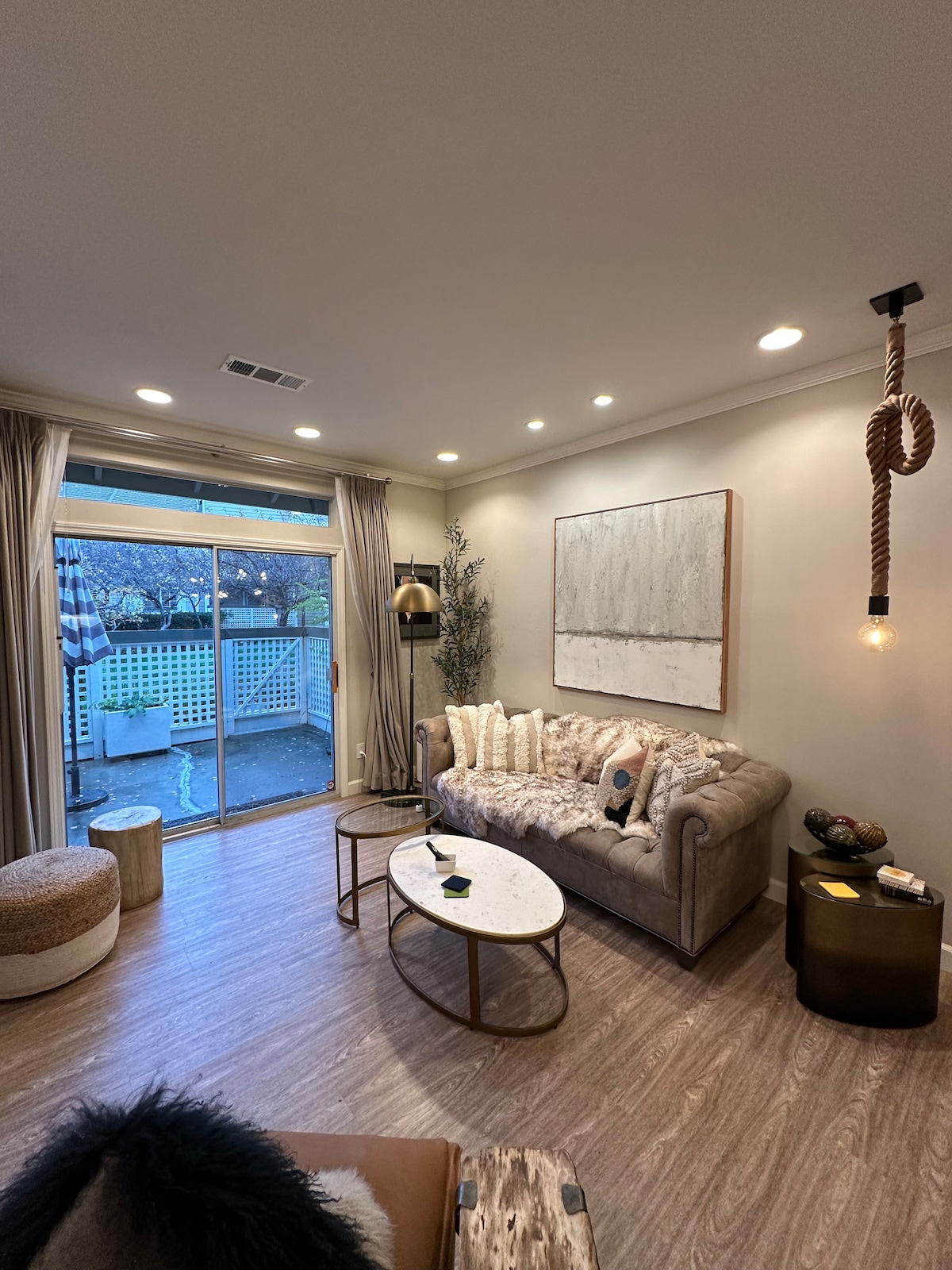 A modern living room features a comfortable sofa adorned with textured cushions, paired with a coffee table of white marble and gold accents. Natural light floods through sliding glass doors that lead to a private fenced-in patio, enhancing the cozy atmosphere.