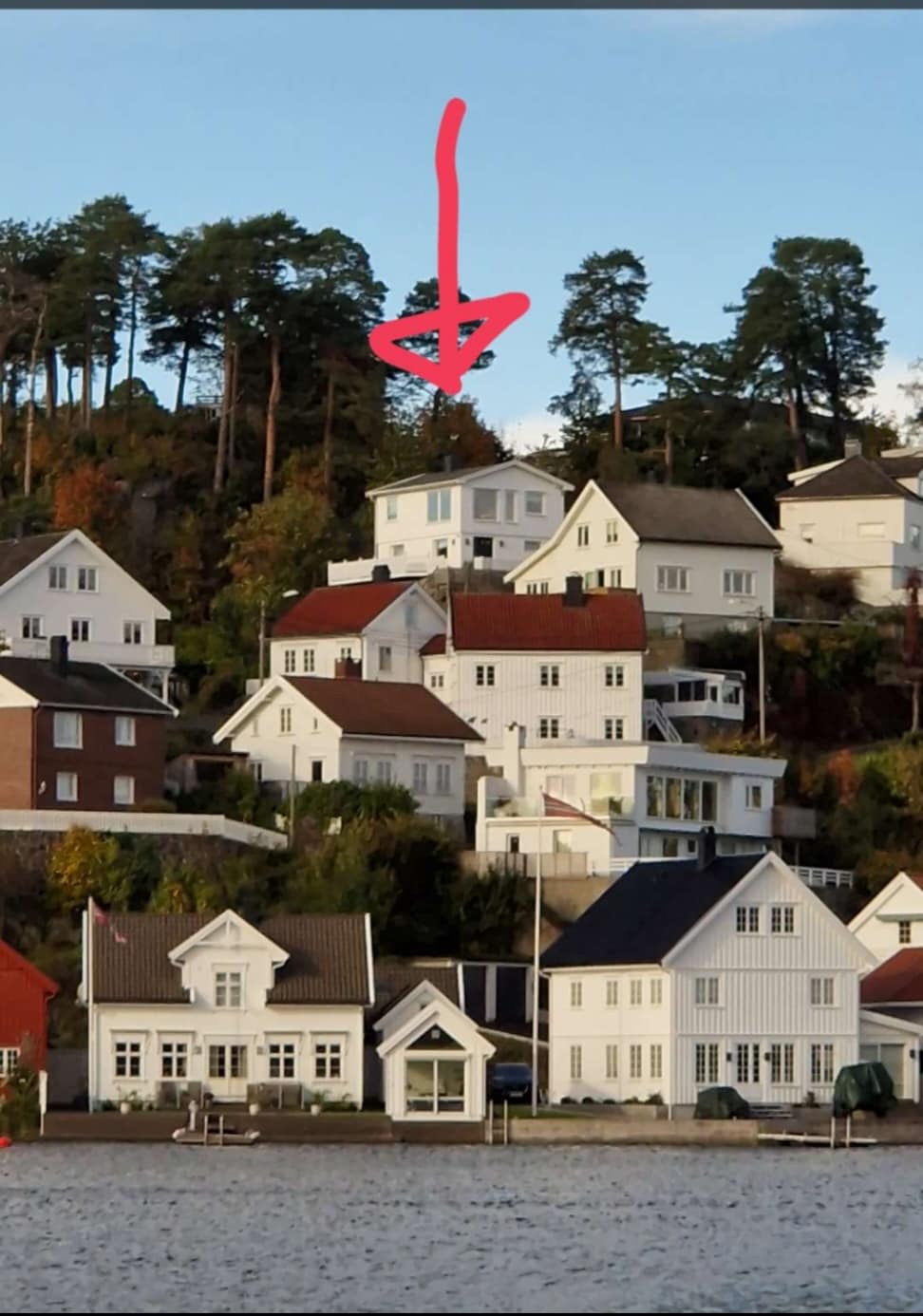A view of a hillside neighborhood is presented, showcasing a collection of residential houses with varying architectural styles. Trees provide a natural backdrop, and the waterway at the base of the hill reflects the surrounding scenery.