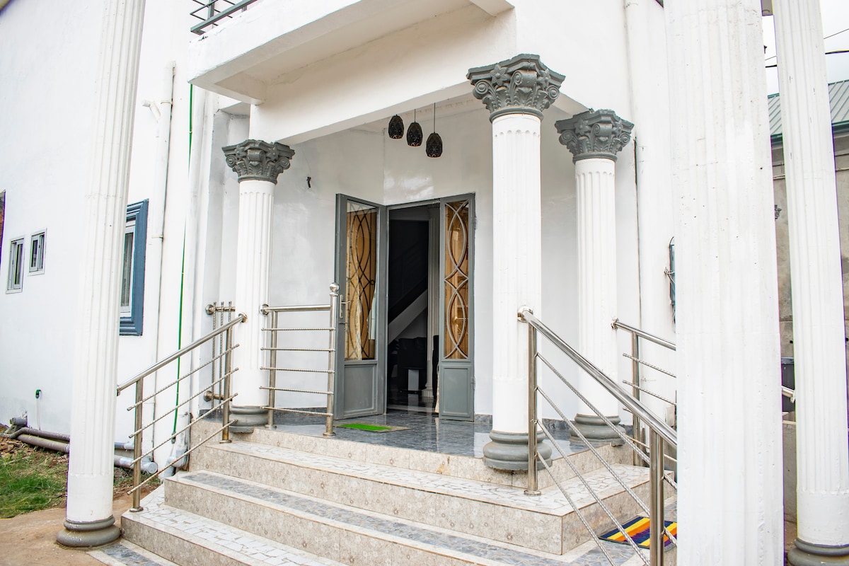 The entrance features a set of grand steps leading to double doors framed by decorative columns. A sleek railing provides support along the pathway, while subtle architectural details enhance the entrance's elegance.