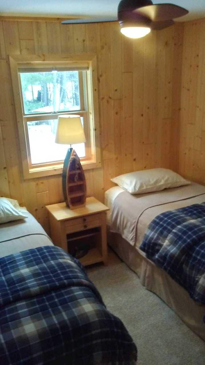 Segundo dormitorio con 2 camas individuales, paredes de pino nudoso y ventilador de techo.