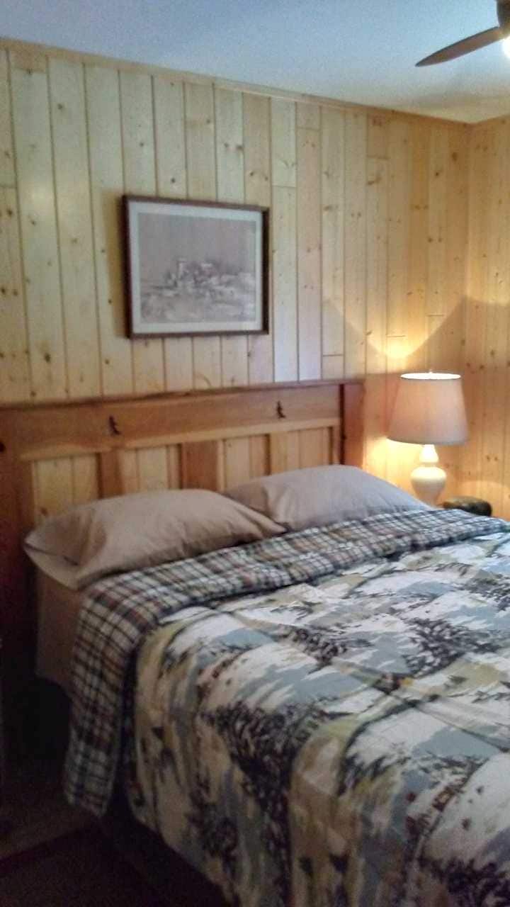 Dormitorio principal con cama tamaño queen, paredes de pino nudoso y ventilador de techo.